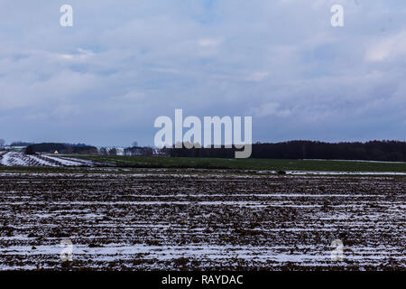 On the plowed field lies a bit of snow. Dark forest surrounds the fields. The beginning of winter in Europe. Stock Photo