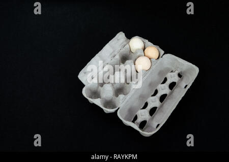 Cardboard egg box with three eggs on black felt background. Stock Photo