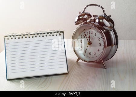 Vintage alarm clock with an empty notebook on a desk. With copy space for your own text. Stock Photo