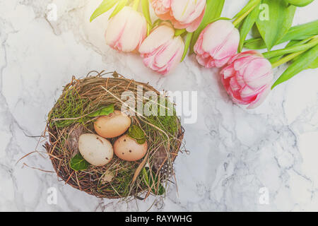 Spring greeting card. Easter eggs in nest with moss and pink fresh tulip flowers bouquet on marble background. Easter concept. Flat lay top view copy space. Spring flowers tulips Stock Photo