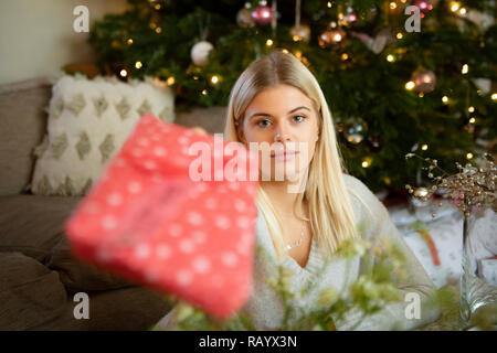 A pretty girl passes a Christmas present from under the Christmas tree Stock Photo