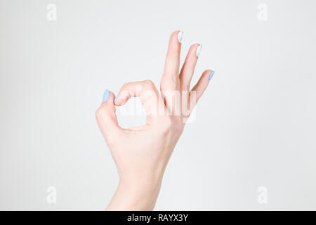 Closeup view of white female hand in ok gesture isolated on white background. Fingernails with modern gel polish manicure of white and blue colors. Stock Photo