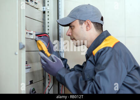Electrician at work using a tester on an industrial panel in a factory Stock Photo