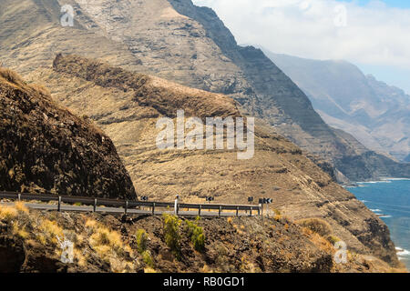 Road trip views on a coastal road with huge mountain ranges in the background right next to the sea / Atlantic ocean (Gran Canaria, Spain, Europe) Stock Photo