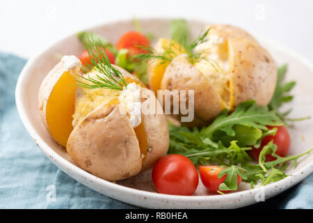 Baked potatoes with sour cream and cheese served with arugula tomato salad. Closeup view Stock Photo