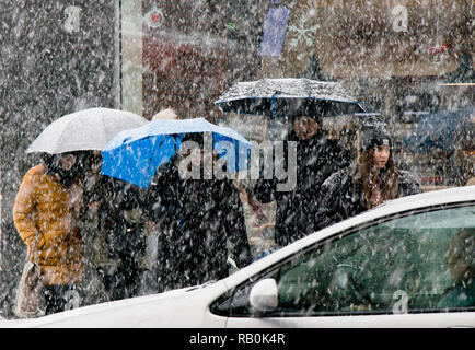 Belgrade, Serbia - December 15, 2018: People under umbrellas crossing snowy city street in heavy snowfall and a driving car in front of them Stock Photo