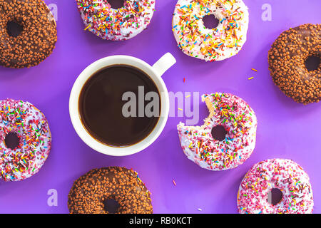 Delicious glazed donuts and cup of coffee on violet surface. Flat lay minimalist food art background. Top view. Stock Photo