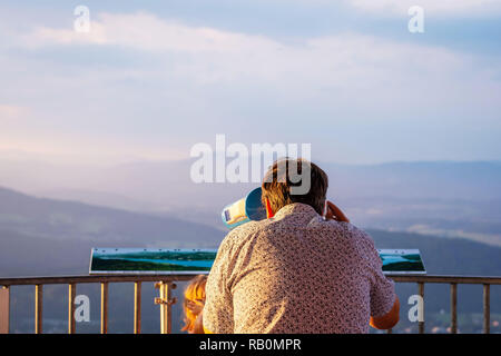 The man from the observation tower  in Coin-operated binoculars looks at the mountains. View from back. Stock Photo
