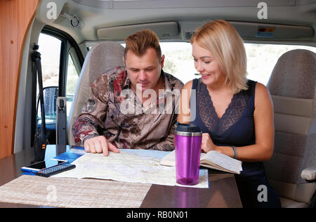 Middle aged married couple talking about future adventure planning route looking at map sitting inside of recreational vehicle motor home trailer. Stock Photo