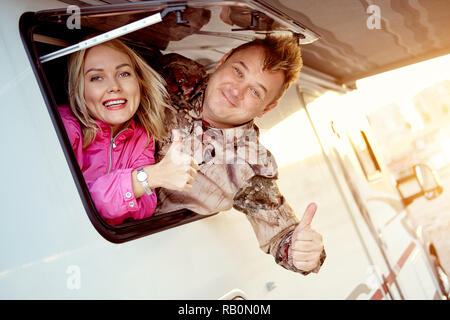 Married middle-aged couple family show thumbs up finger up getting out from caravan recreational vehicle motor home trailer window looking at camera Stock Photo