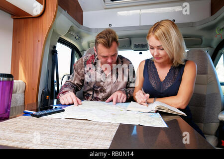Middle aged married couple talking about future adventure planning route looking at map sitting inside of recreational vehicle motor home trailer Stock Photo