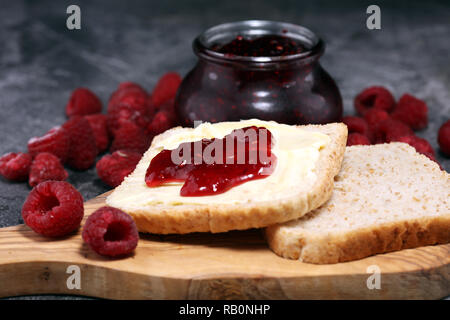 Toast bread with homemade raspberry jam or marmalade on rustic table served with butter for breakfast or brunch. Stock Photo