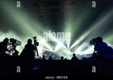 Silhouette of a group of cameramen broadcasting an event. Workers are on a high platform on the background of bright beams. Stock Photo