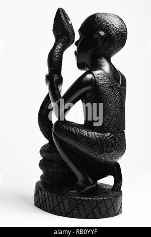 Wooden African figure art iron wood carving sculpture. Man, in squatting position raised one's hand and holding the snake. 8×7×9 cm. From behind. Stock Photo
