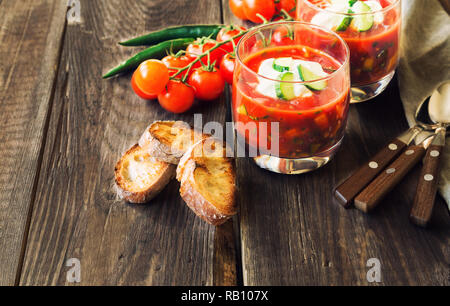 Homemade tomato soup gazpacho in glasses with toasted bread on rustic wooden background. Healthy food. Spanish cuisine. Stock Photo
