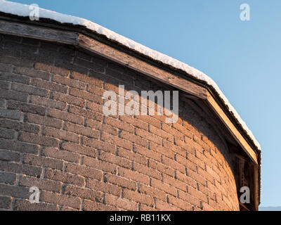 Snowy roof over curved grey brick wall with light gradient. Stock Photo