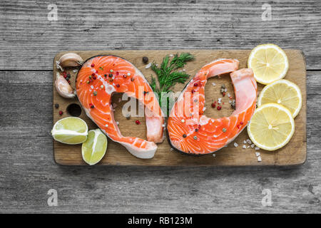 raw salmon steak with herb, lemon and peppercorns on wooden cutting board. healthy and diet food. top view Stock Photo