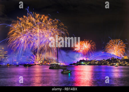 Calligraphic drawing in dark midnight sky of Sydney city during New year fireworks with splashes of colourful light balls over harbour water, CBD towe Stock Photo