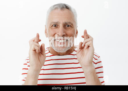 Unaltered shot of hopeful charismatic and happy optimistic senior retired man in striped t-shirt crossing fingers for good luck smiling broadly while making wish hoping for dream come true Stock Photo