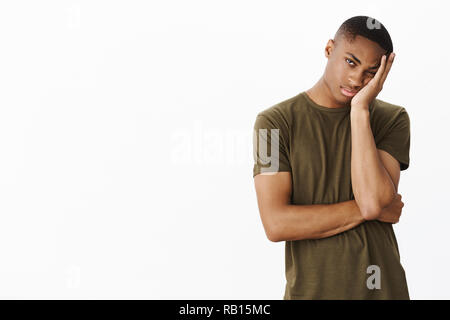 Guy hates long queues. Bored and indifferent attractive young african american male making face palm, leaning head on hand peeking with one eye at camera apathic and tired over white background Stock Photo