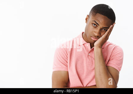 How long it lasts. Bored and indifferent displeased young african american male student leaning face on palm looking at camera with boredom and apathy feeling tired posing over gray background Stock Photo