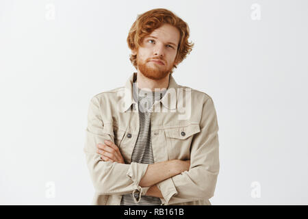 Unimpressed bored and tired male customer thinking and counting how much new purchase will cost being dissatisfied holding hands crossed on chest looking up with indifferent bothered expression Stock Photo