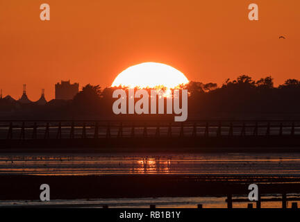 Disappearing sun over trees by the sea in Autumn on the South Coast of the UK. Stock Photo