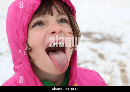 Portrait of a young girl in the snow trying to catch a snowflake on her tongue Stock Photo