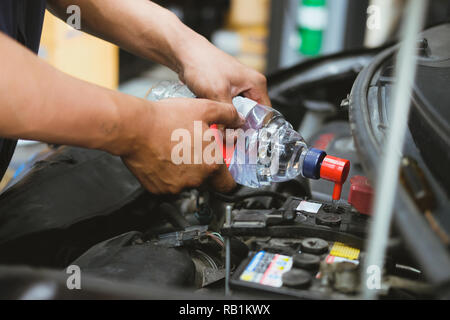 mechanic pouring distilled water to fill car battery in automobile repair service garage Stock Photo
