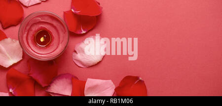 Candle and rose petals on red background. Banner format. Stock Photo