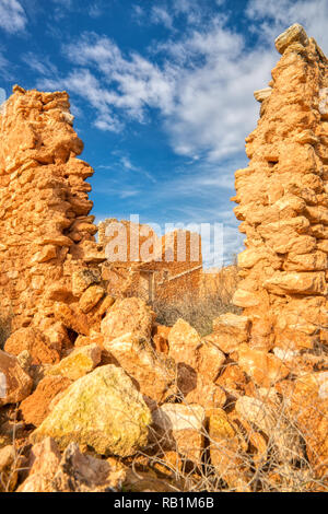 A vertical photo of the ruins of an old stone house looking through a broken part of the wall at another part of the house with a blue sky and clouds