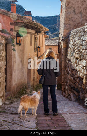 A blonde woman looking down a random cobblestone Spanish street in the small town of Albarracin with her blonde border collie mix dog and a hint of su Stock Photo