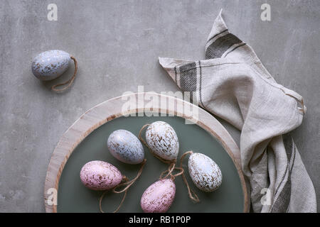 Top view of decorative Easter eggs in pastel colors on decorative tray with linen towel on light stone background Stock Photo
