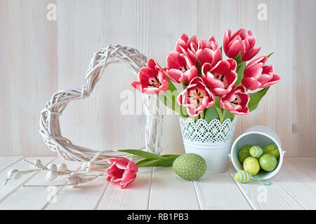 Springtime background with pink stripy tulups, Easter eggs and wattled heart on light wooden background. Stock Photo