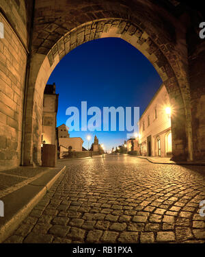 Romantic Prague at dawn, entrance to Charles Bridge through the illuminated arch of Lesser Town Bridge Tower early in the morning. Panoramic image, sq Stock Photo