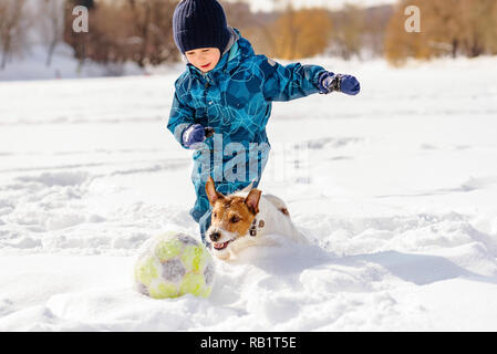 4 years old boy playing football (soccer) with his dog on snow Stock Photo