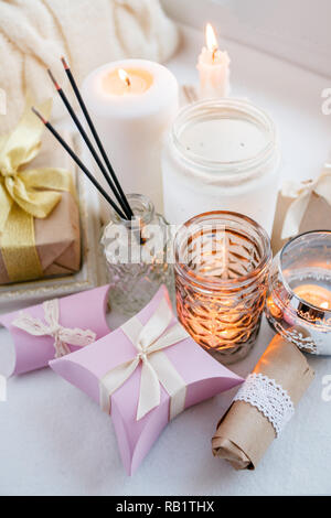 paraffin wax candles and one tealight in a glass candle holder and aroma stick, romantic gift boxes, standing on a windowsill early morning, concept o Stock Photo