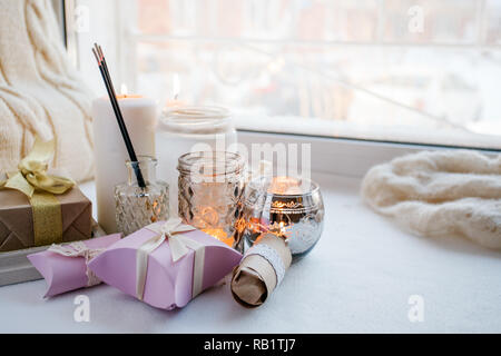 paraffin wax candles and one tealight in a glass candle holder and aroma stick, romantic gift boxes, standing on a windowsill early morning, concept o Stock Photo