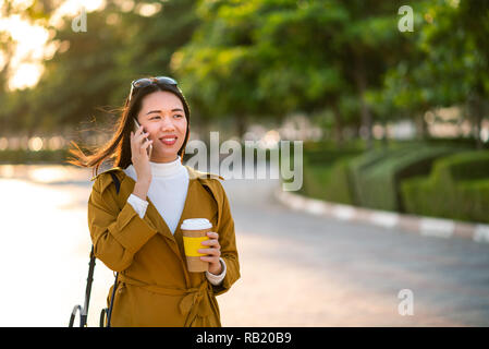 Cheerful girl using phone and having a cup of coffee outdoors Stock Photo