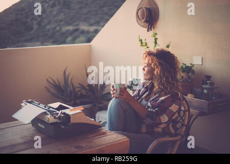 Evening with lovely light and beautiful lonelyh woman taking and drinking a tea with old typewriter no technology in front on the table - alernative l Stock Photo