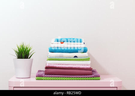 On the dresser there is a stack of clean ironed bed linen, folded multi-colored towels and a home plant stands. Stock Photo
