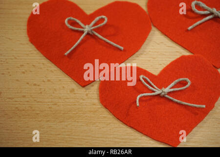 Three red hearts made from textile decorated with linen rope bow on wooden background Stock Photo