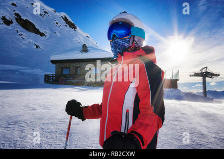young boy on ski slope with goggles and reflection of snowed mountains on the mask. Portrait of skier at the ski resort with mountain shelter and snow Stock Photo