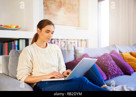 Portrait of beautiful young woman typing on laptop while working from home. Stock Photo