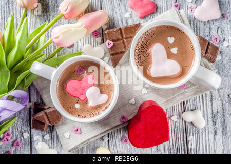 Valentines day treat ideas, two cups hot chocolate drink with marshmallow hearts red pink white color with chocolate pieces, sugar sprinkles, old wood Stock Photo