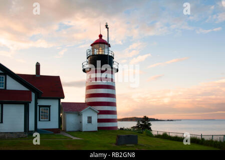 Old striped lighthouse tower of West Quoddy Head light shines brightly during sunset in northern New England. It uses an authentic Fresnel lens and is Stock Photo