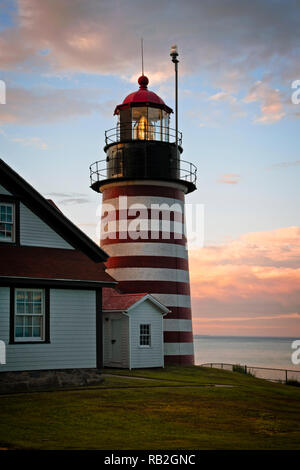 Authentic fresnel lens of West Quoddy head lighthouse, famous for its red and white srtipes, shines brightly during sunset in northern New England. It Stock Photo