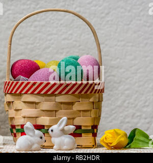 Easter basket filled with plastic eggs rolls and two white bunnies against white background decoreated with yellow tulip and plenty of copyspace Stock Photo