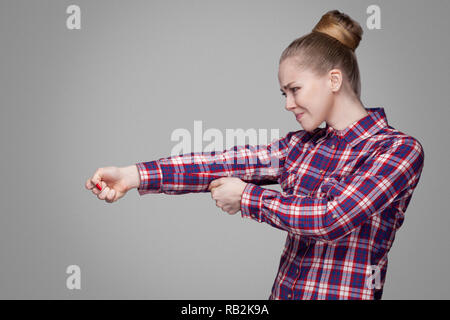 profile side view of blonde girl in red, pink checkered shirt, collected bun hairstyle standing and fists with srious face or try to pulling. indoor s Stock Photo