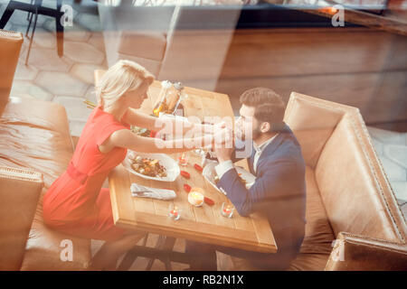 Young man and woman on date in restaurant sitting at table eating vegetable salad man holding hands of woman kissing joyful reflection top view Stock Photo